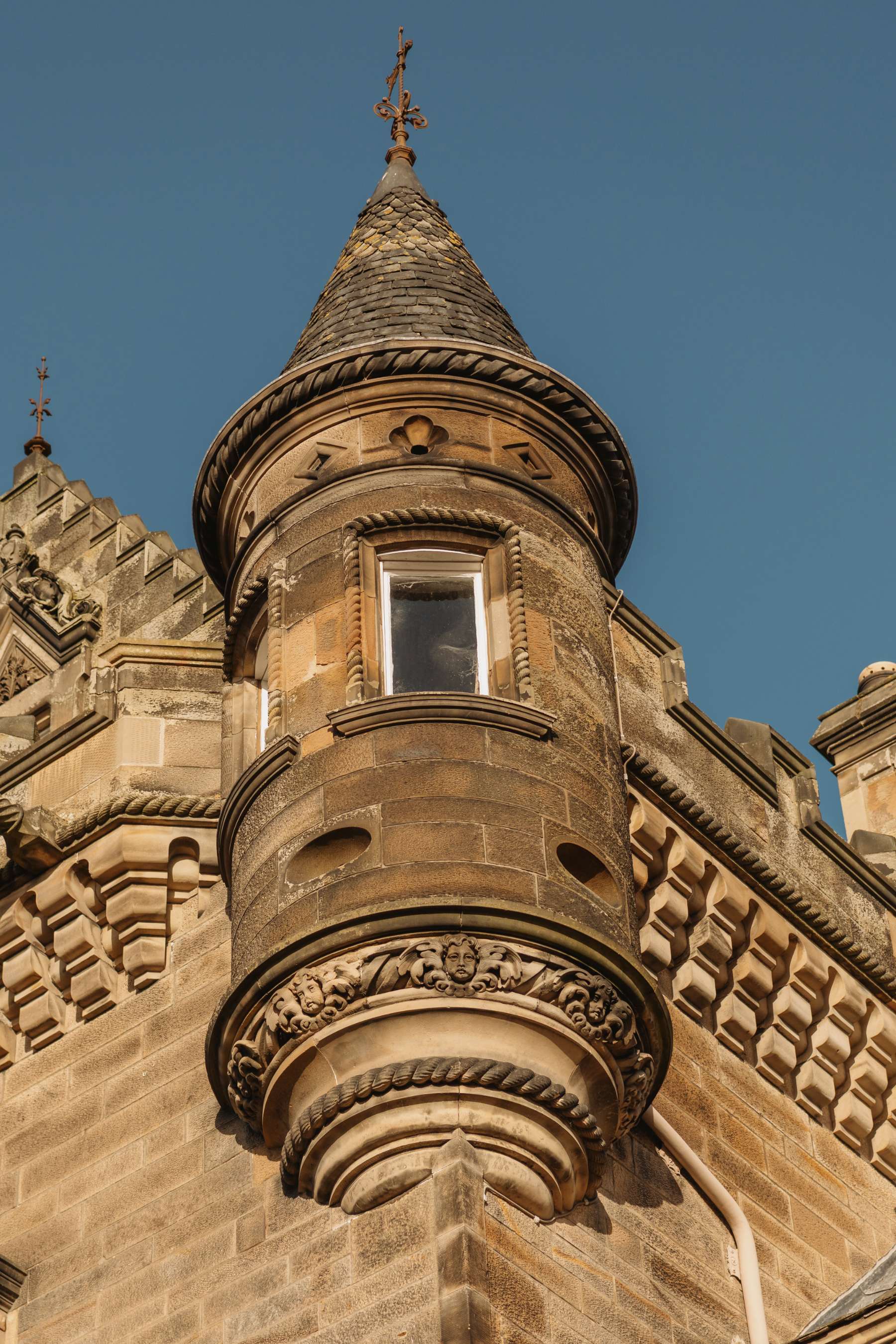 A conical-roofed stone turret with a small window stands against a clear blue sky.