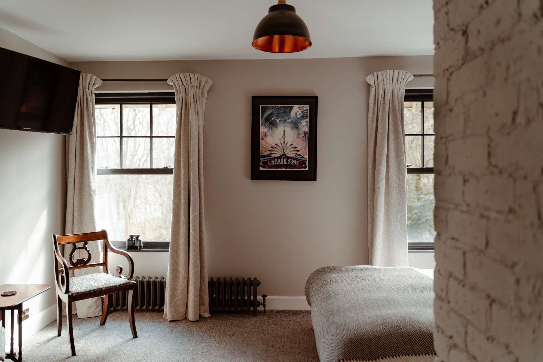 A vintage travel poster for Argyllshire hangs on a pale wall between two curtained windows, a wooden chair and radiator beneath.
