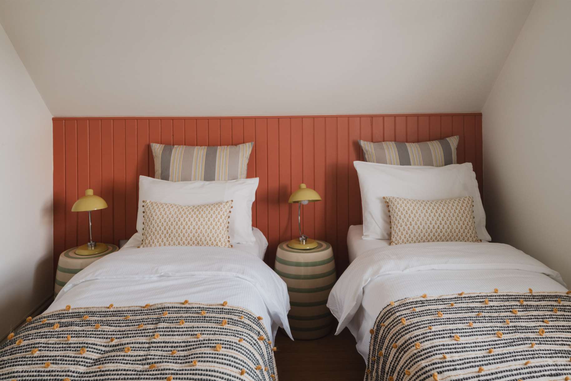 Twin beds with striped throws sit against a terracotta panelled wall, matching lamps lit on the shared bedside table.
