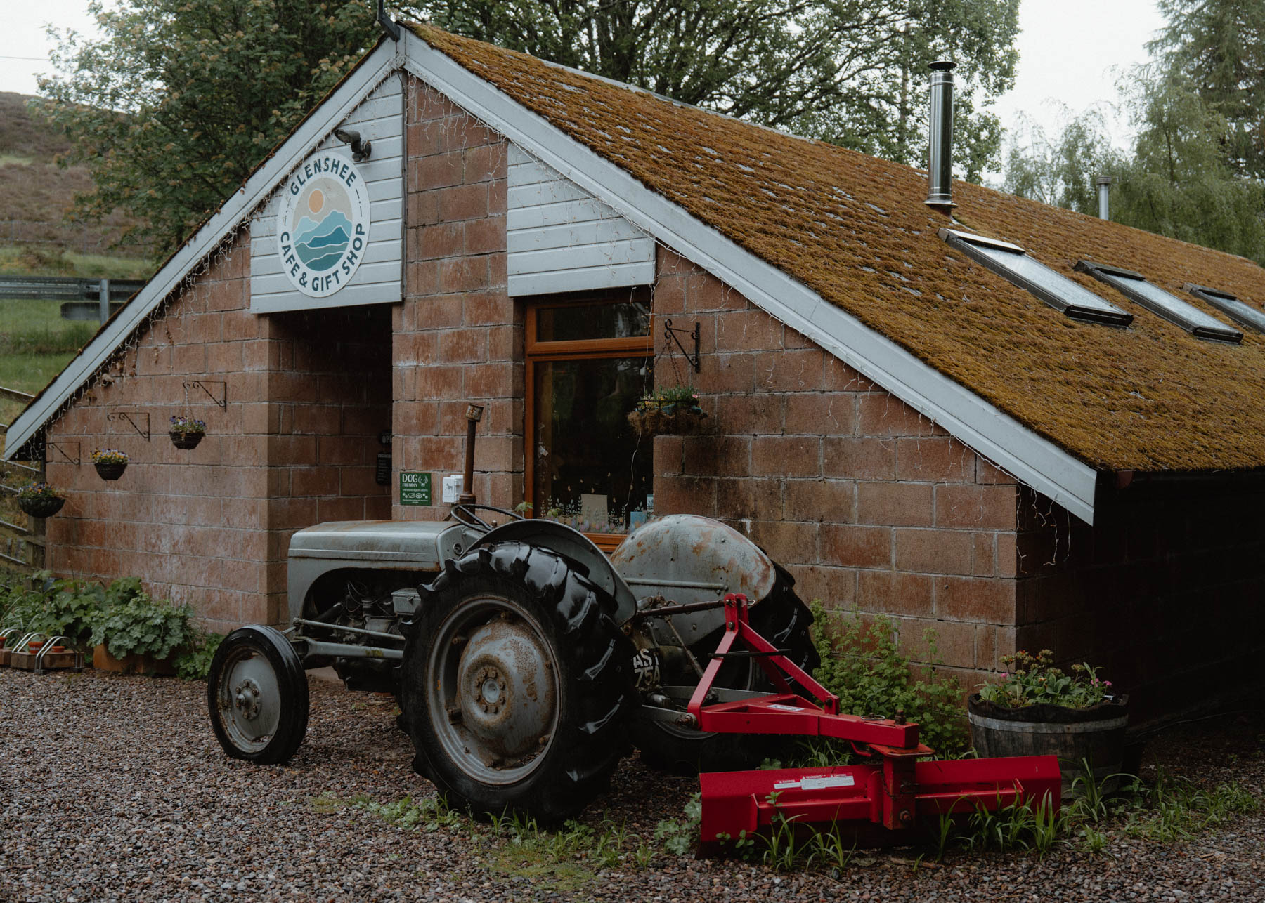 Glenshee Café's brick building with its round sign and an old grey tractor outside.