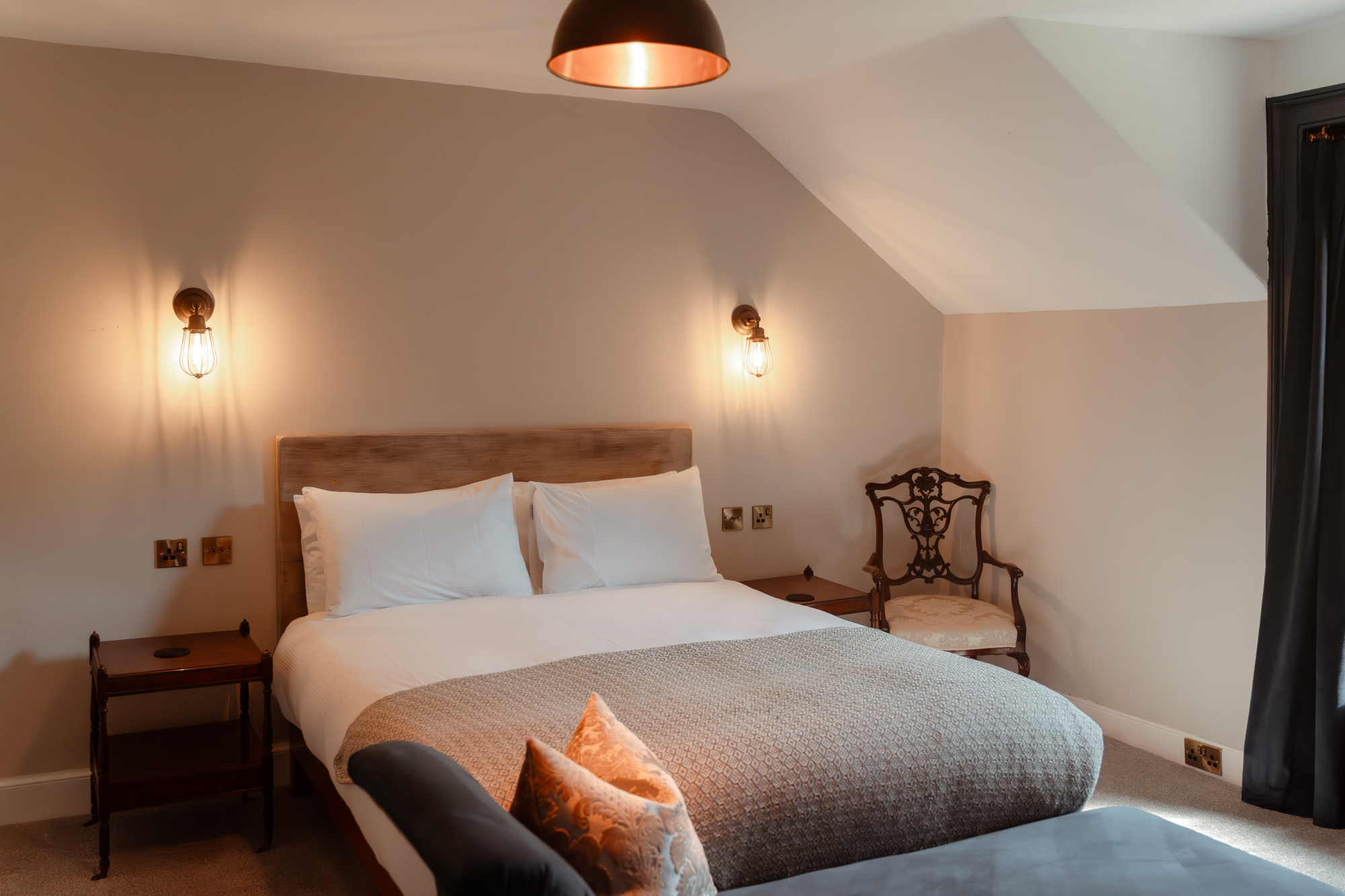 A single bed with teal cushions sits beneath framed art, a stone chimney breast and radiator in the foreground of the room.