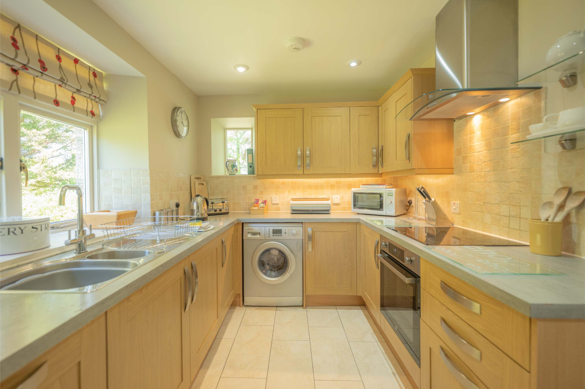 A fitted kitchen with pale wood units and a stainless steel extractor hood, a washing machine and oven built in beneath the counter.