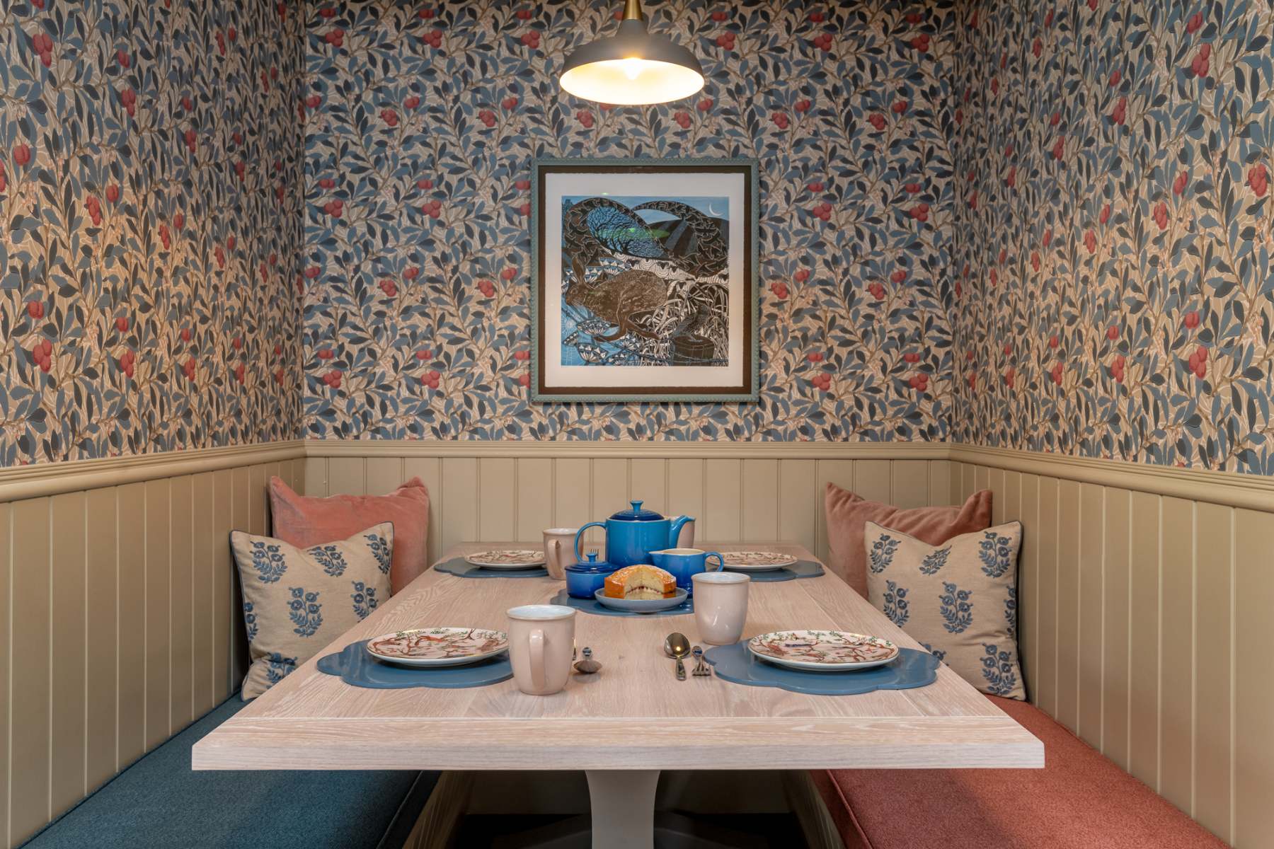 A breakfast nook is set with a jug and plates beneath a framed print of a loch.