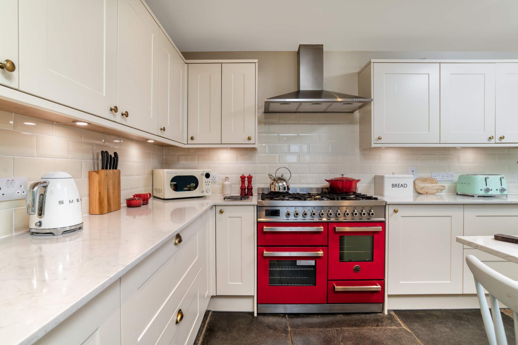 A red range cooker sits below an extractor hood in a white kitchen, a kettle and toaster on the worktop to the side.