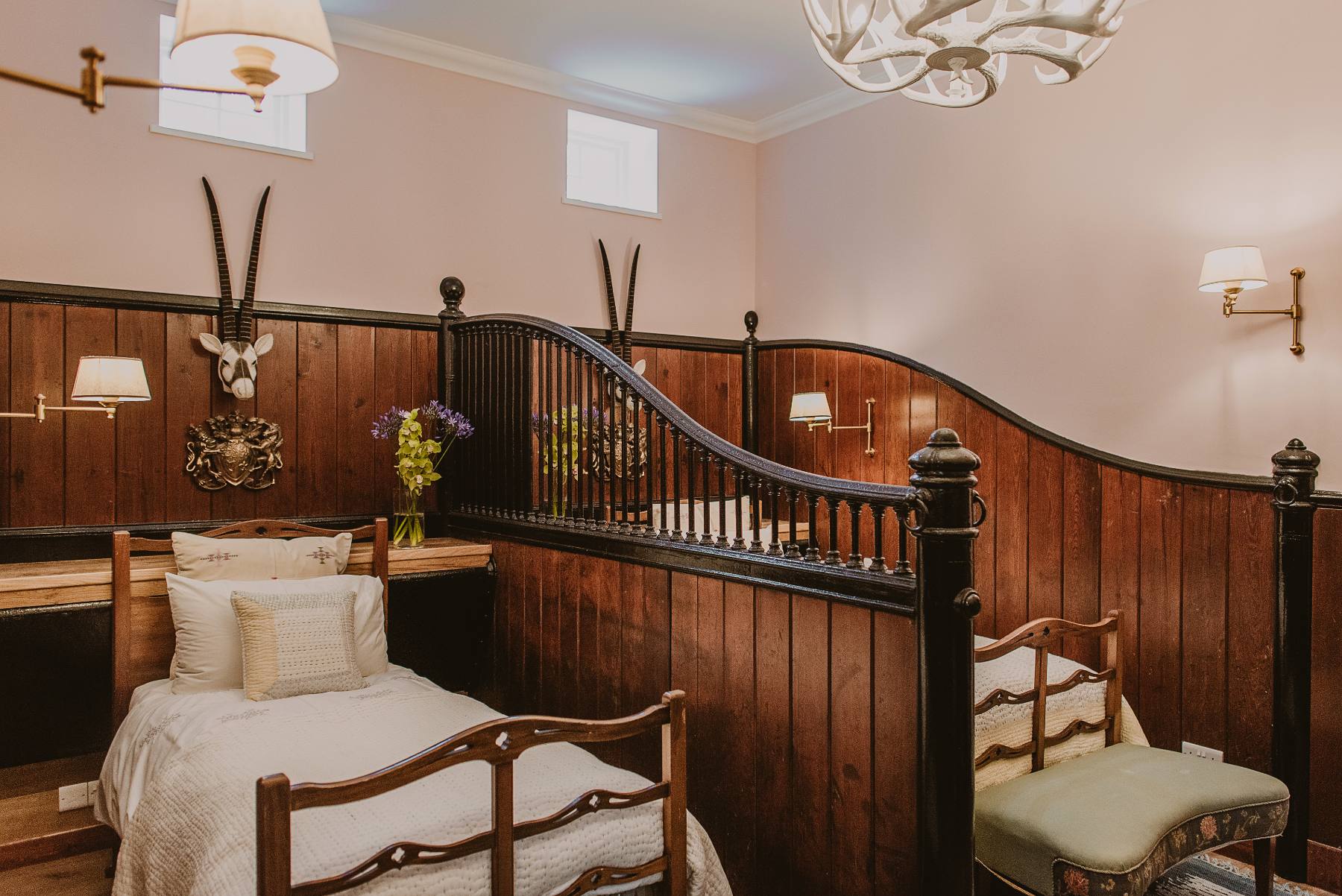 A curved dark wood staircase rail rises beside a panelled wall, a single bed and a bench with a green cushion in the foreground.