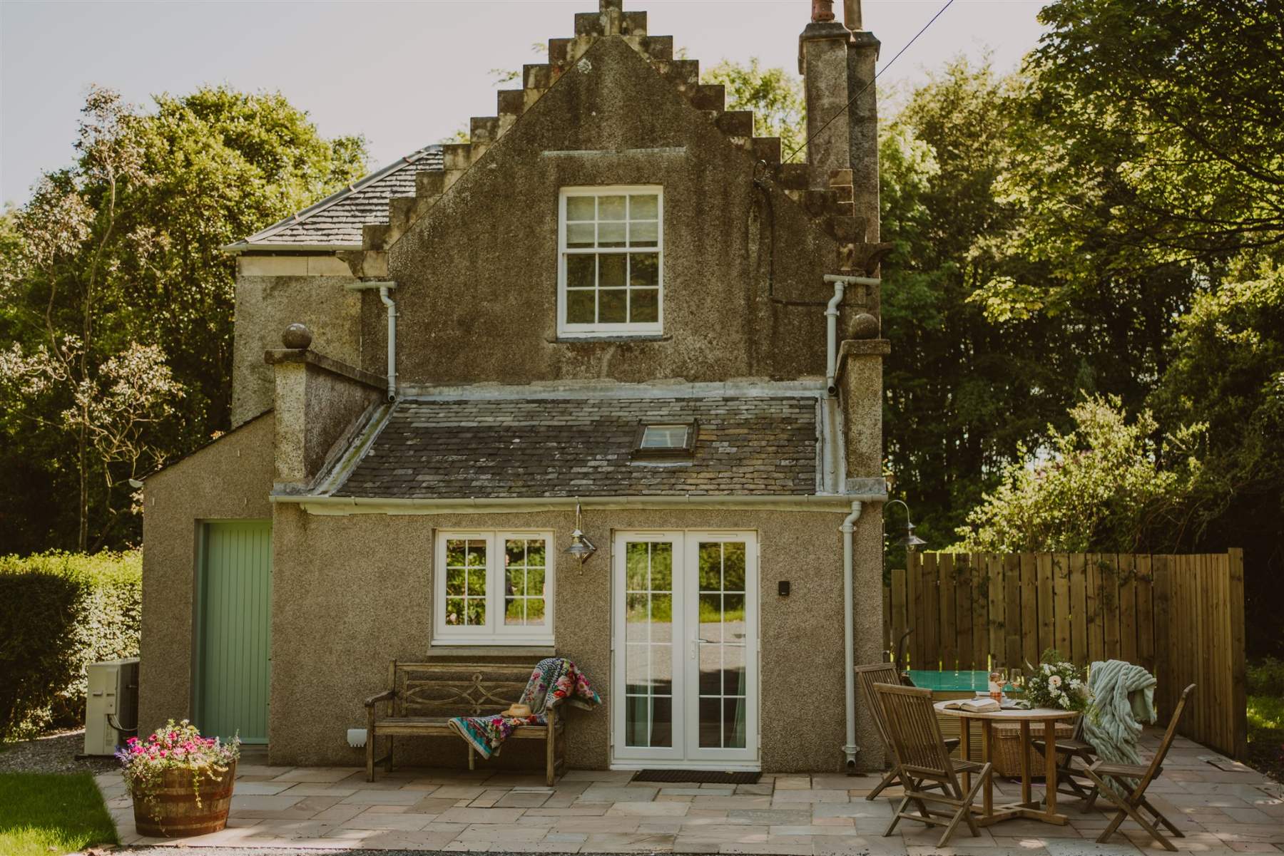 The stone cottage seen from the garden, with crow-stepped gables, a wooden bench and a hot tub set on the patio to the right.